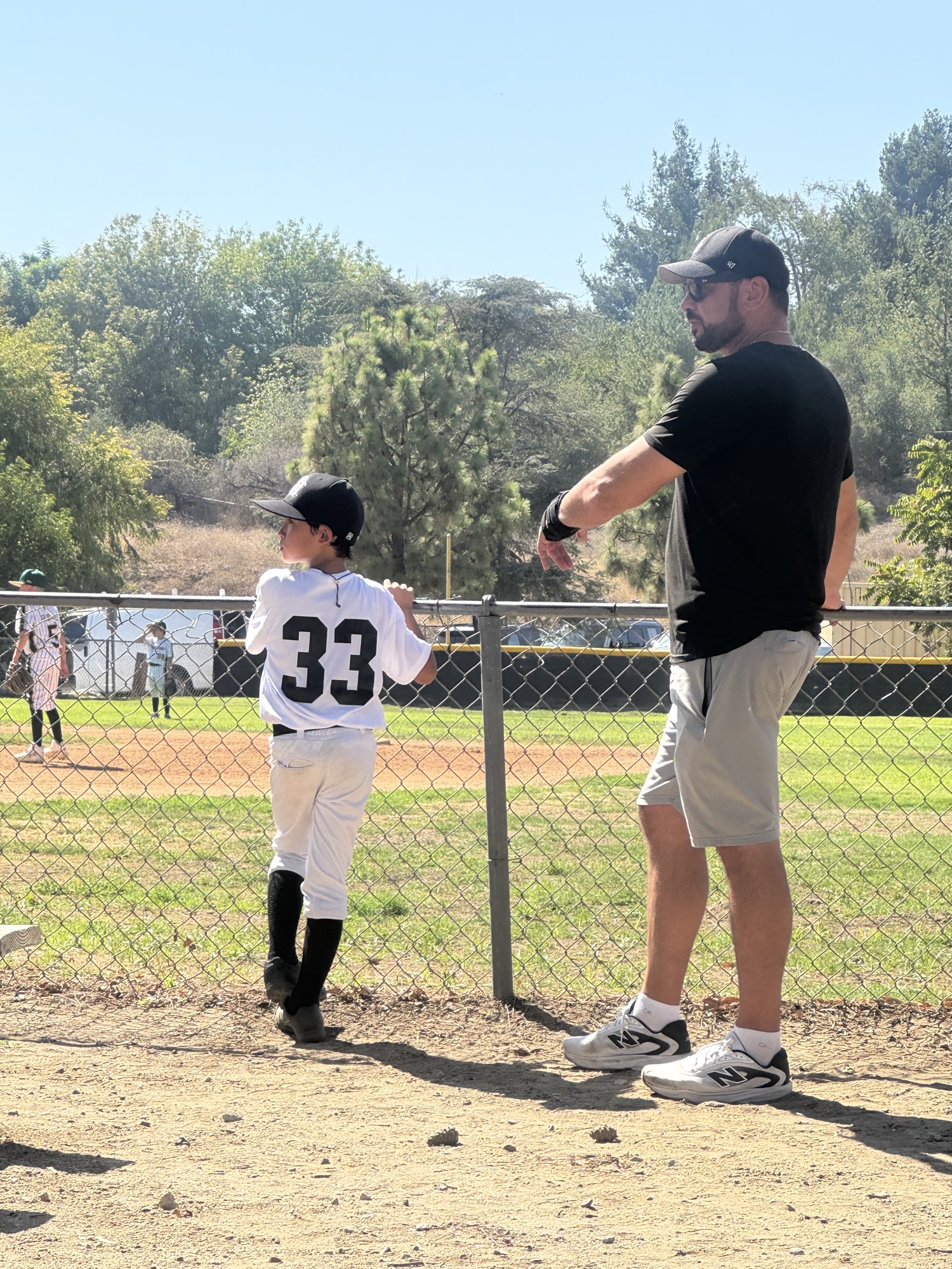 Roland coaching Koji, number 33, at the fence during a game